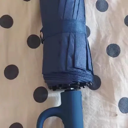 Folded navy Umbremo umbrella lying on a bed, close-up of the handle and strap